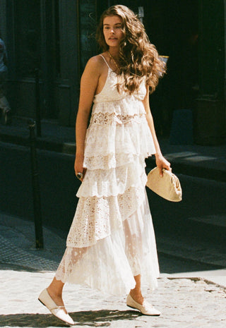 A woman walking outdoors in a white lace and tulle maxi dress with a tiered ruffle design