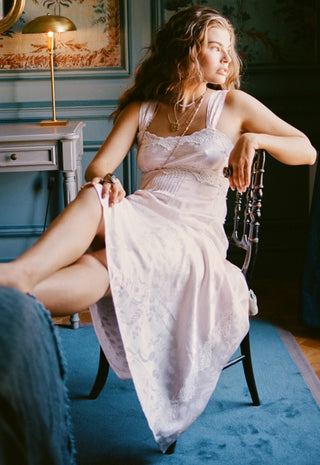 A woman reclining on a dark wooden chair in a vintage-style room